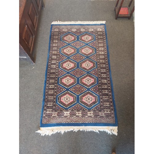 1019 - A blue and pink ground wool and cotton rug with diamond lozenges and geometric border, 165cm x 95cm