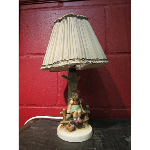 4130 - A Goebel table lamp, girl perched on fence with basket, pleated shade, loss to hair