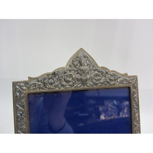 4461 - A Thai white metal photograph frame with allover repousse design and deity to top, 18cm x 12.5cm ape... 