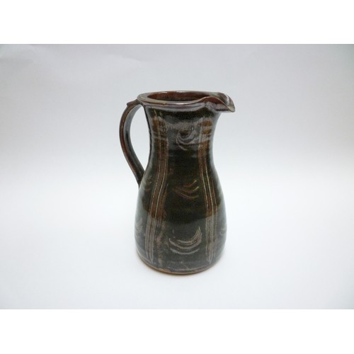 1317 - A tall Winchcombe studio pottery stoneware jug. Tenmoku glaze and finger wipe detail. Seal under str... 