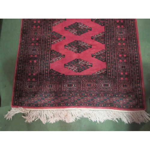 4106 - A Pakistan wool rug, dark pink ground with green and white motif, multiple borders, tasselled ends, ... 