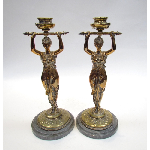 7644 - A pair of brass candlesticks as robe clad females, upon grey marble plinth bases, 30cm high