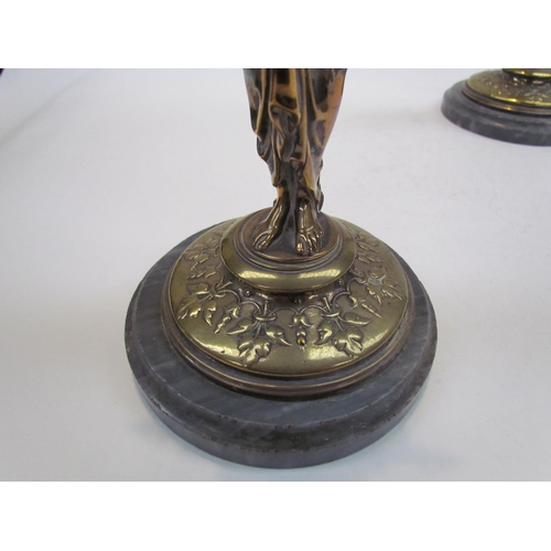 7644 - A pair of brass candlesticks as robe clad females, upon grey marble plinth bases, 30cm high