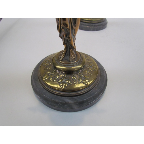 7644 - A pair of brass candlesticks as robe clad females, upon grey marble plinth bases, 30cm high