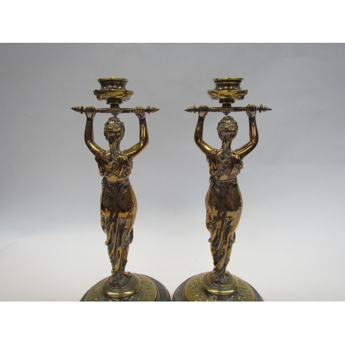 7644 - A pair of brass candlesticks as robe clad females, upon grey marble plinth bases, 30cm high