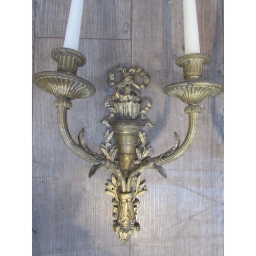 7021 - A pair of cast gilded twin branch candle wall lights with ribbon and acanthus detail, 36cm tall