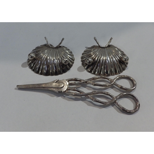 7208 - A pair of silver grape scissors with branch effect handles and two white metal scallop form dishes, ... 