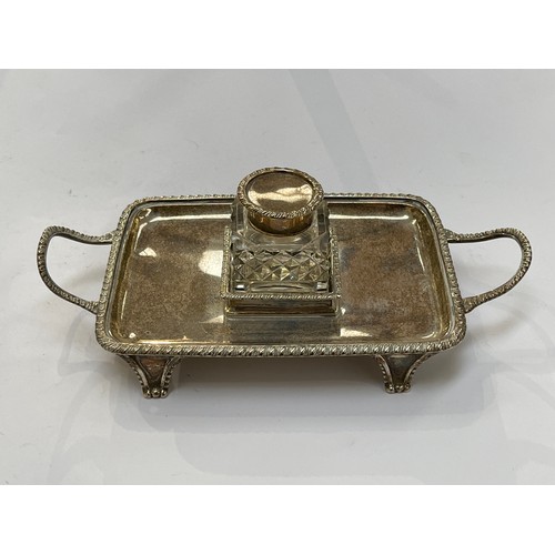 7309 - An Edwardian silver desk stand, twin handle, gadrooned border, central inkwell, raised on feet, make... 