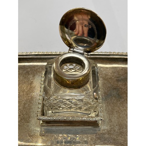 7309 - An Edwardian silver desk stand, twin handle, gadrooned border, central inkwell, raised on feet, make... 