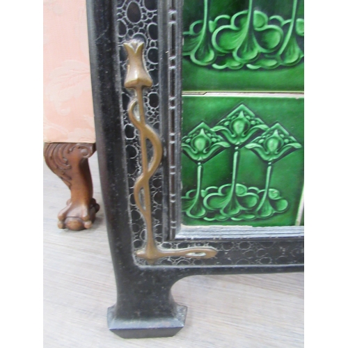 7823 - An Art Nouveau fire screen, the scrolled brass top over a black metal frame, green tiled centre, 76c... 