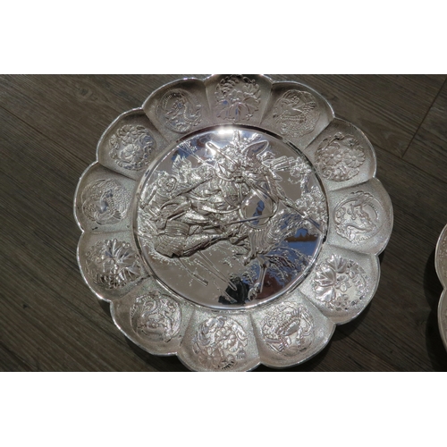 7471A - A pair of white metal scalloped form chargers with centres depicting Japanese warriors, 31cm diamete... 