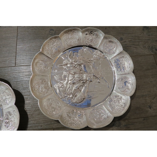 7471A - A pair of white metal scalloped form chargers with centres depicting Japanese warriors, 31cm diamete... 