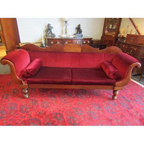 1033 - A Victorian scroll end sofa on turned legs with castors with red velour upholstery and bolster cushi... 