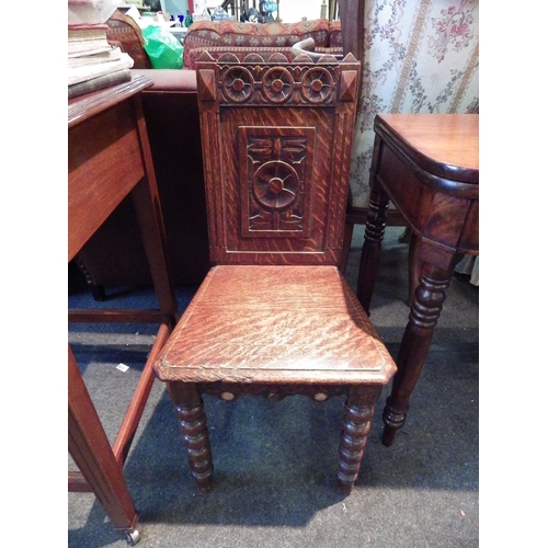 1150 - An oak hall chair with heavily carved back, raised on turned legs