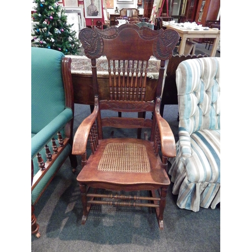 1155 - An Arts & Crafts carved oak rocking chair with ring turned spindle supports and cane seat