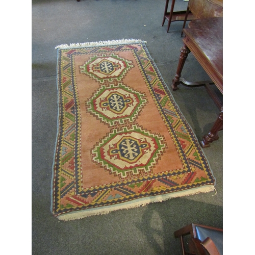 1481 - A peach and cream ground geometric design rug, three central lozenges, multiple borders and tasselle... 