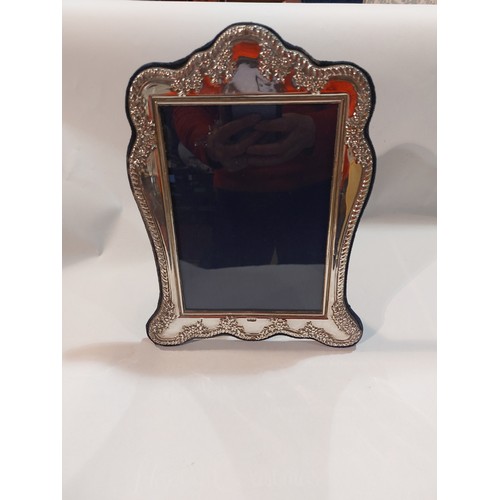 4372 - A silver photograph frame with embossed floral decorated shaped edge, easel back. Hallmarked 1998 ma... 