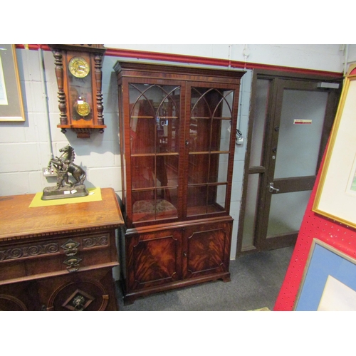 1036 - A George III style flame mahogany two door glazed bookcase over a two door cupboard on outswept brac... 