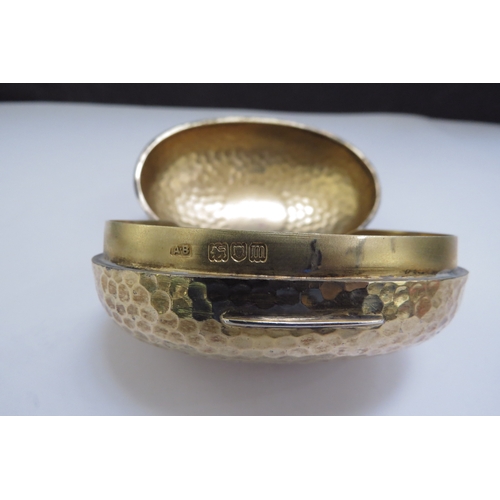 6438 - An Albert Barker Ltd silver gilt hinged ovoid shaped box with hammered decoration, circular cartouch... 