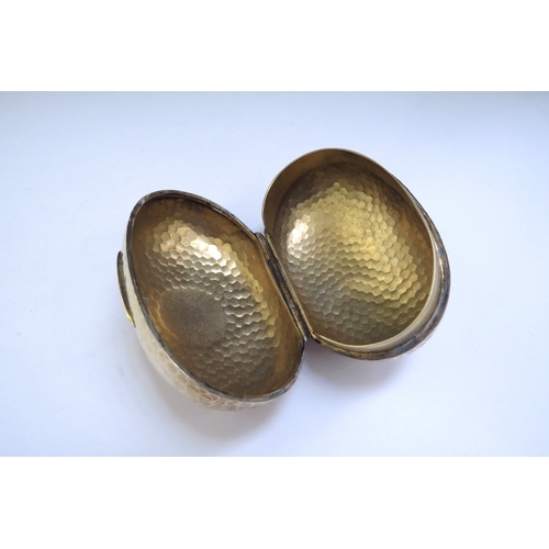 6438 - An Albert Barker Ltd silver gilt hinged ovoid shaped box with hammered decoration, circular cartouch... 