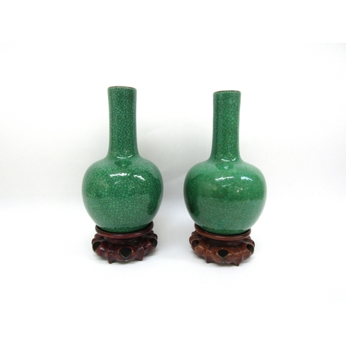 6345 - A pair of Chinese apple-green crackle-glazed bottle vases on carved wooden stands, label to inside o... 