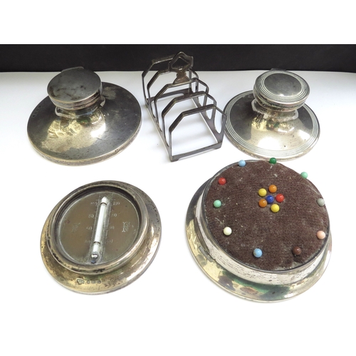 6412 - Two silver capstan inkwells, a pincushion, desk thermometer and a five bar toast rack (5)