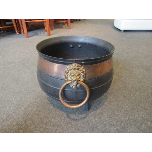 1001 - A cast iron cauldron with copper banding, lion mask ring handles and on tripod feet, 35cm diameter, ... 