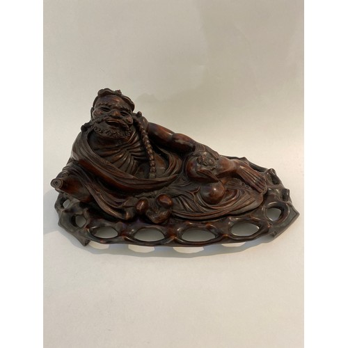 6338 - A Chinese carved figure of an Immortal resting on a carved bespoke base, 21cm x 41.5cm