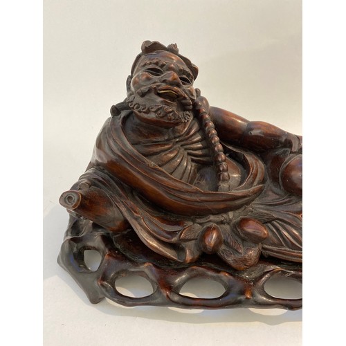 6338 - A Chinese carved figure of an Immortal resting on a carved bespoke base, 21cm x 41.5cm