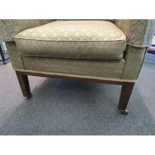 1109 - An early 20th Century armchair, square arms, green patterned upholstery, on square legs to castors