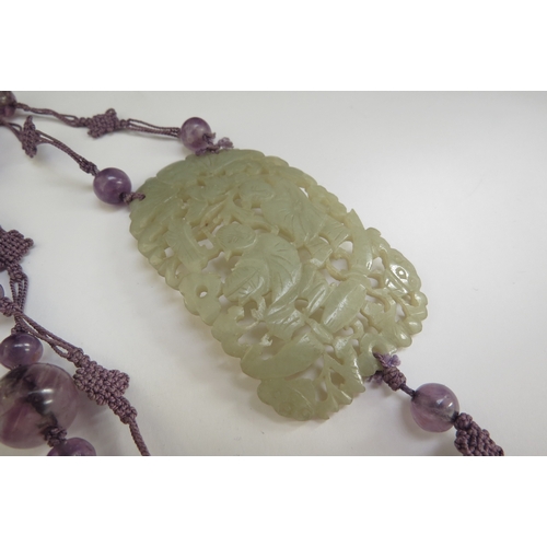 7068 - A jade carved and pierced panel depicting figures in foliage 7cm x 4cm on an amethyst bead and purpl... 