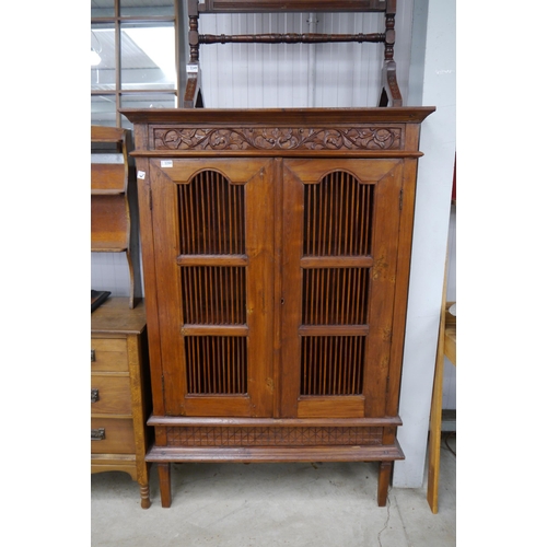 2250 - An Indonesian hardwood cabinet, scrolled foliate carved rail painted in colours, grilled doors, rais... 