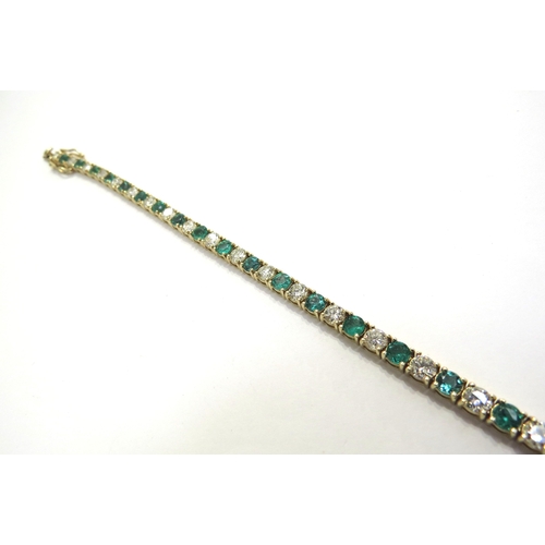 7039 - An emerald and diamond line bracelet all in four claw mounts, having 22 alternate set emeralds (3.74... 