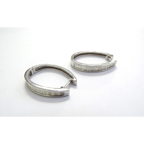 7057 - A pair of white gold elongated hoop earrings, the front half with a line of baguette diamonds, hinge... 