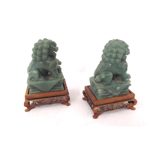 5046 - A pair of Chinese carved jade figures of dogs of fo on carved footed stands, 12.5cm tall