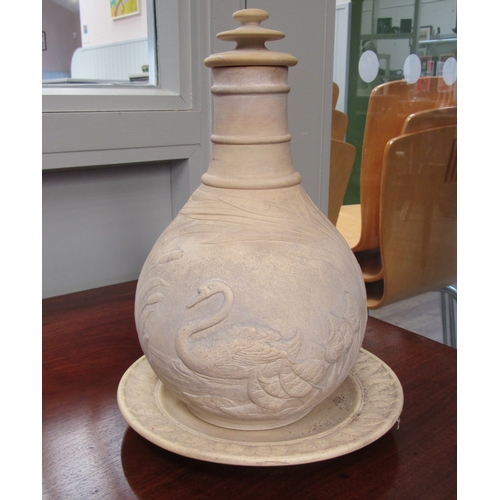 4036 - A cream pottery lidded vessel decorated with raised images of Swans in bulrushes and a saucer, 26.5c... 