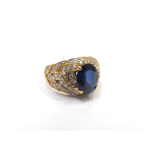 9279 - A yellow gold ring set with a single oval sapphire with flame style milgrain edge patterned mount se... 