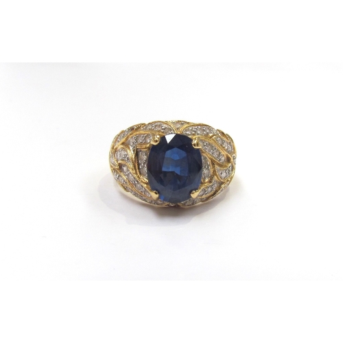 9279 - A yellow gold ring set with a single oval sapphire with flame style milgrain edge patterned mount se... 