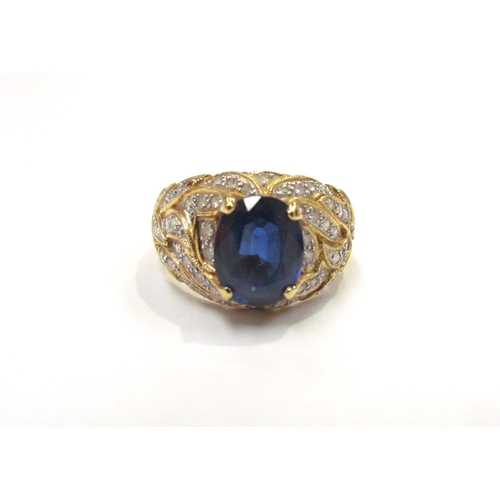 9279 - A yellow gold ring set with a single oval sapphire with flame style milgrain edge patterned mount se... 