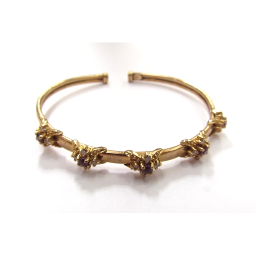 9328 - A 9ct gold bangle with raised floral motifs with amethyst stone centre framed by clear stones, 9.1g ... 