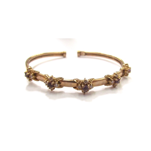 9328 - A 9ct gold bangle with raised floral motifs with amethyst stone centre framed by clear stones, 9.1g ... 