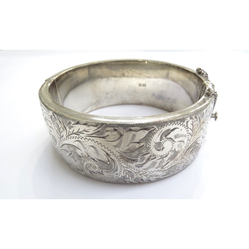 9369 - A silver stiff hinged bangle with engraved decoration, 2.5cm wide, 6cm x 5.5cm opening, 75g