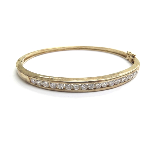 9062 - A 9ct gold stiff hinged bangle with a row of clear stones, 5.3cm x 6cm, 12.2g