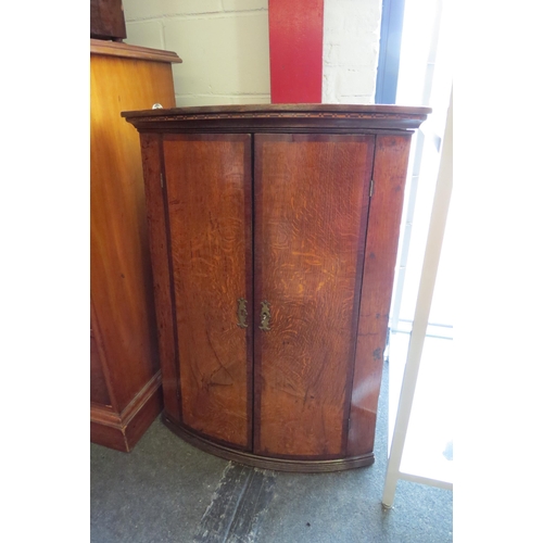 1004 - A George III Lancashire bow front oak two door corner cupboard with mahogany crossbanding and cheque... 