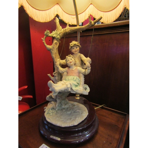 4029 - A B.Merli figural table lamp, boy and girl on swing, fluted and tasselled shade