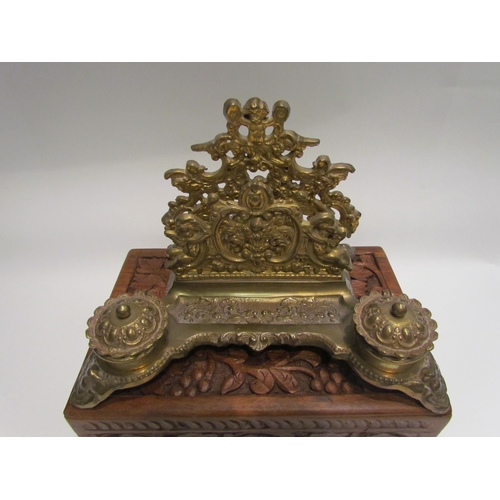 4123 - A gilt brass desk stand with cherubic mounts and twin inkwell, together with a foliate carved hardwo... 