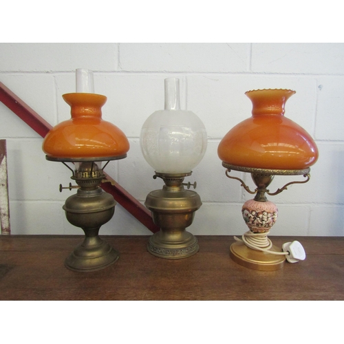 1009 - Two brass oil lamps, one with amber shade and chimney, together with a similar electric adapted lamp... 