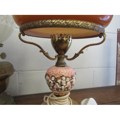 1009 - Two brass oil lamps, one with amber shade and chimney, together with a similar electric adapted lamp... 