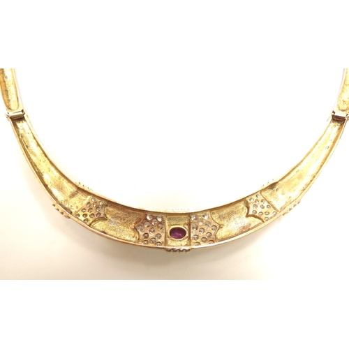 6113 - A gold necklace with articulated long links, centrally set with an oval ruby flanked by clusters of ... 