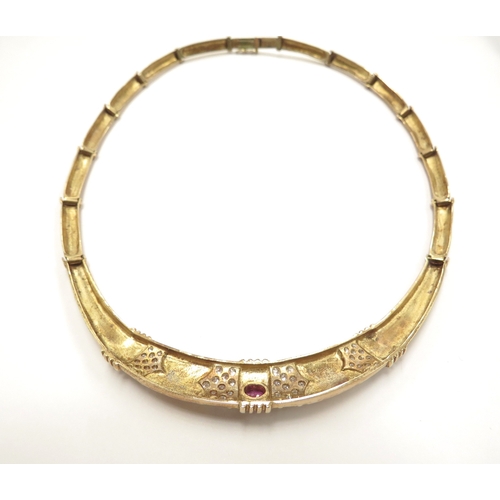 6113 - A gold necklace with articulated long links, centrally set with an oval ruby flanked by clusters of ... 